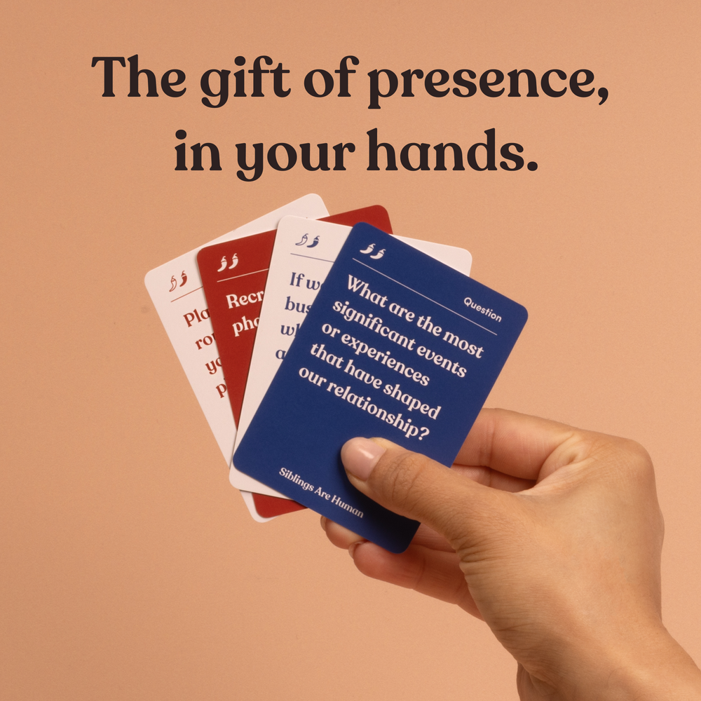 A hand holds fanned Siblings Are Human cards, headline “The gift of presence, in your hands”