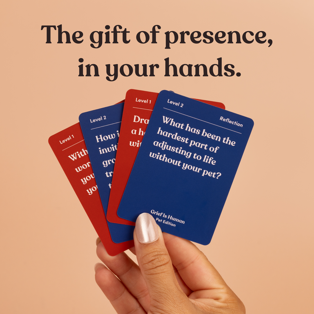 A hand holds a fan of red and blue Grief Is Human Pet Edition cards, headline “The gift of presence, in your hands”