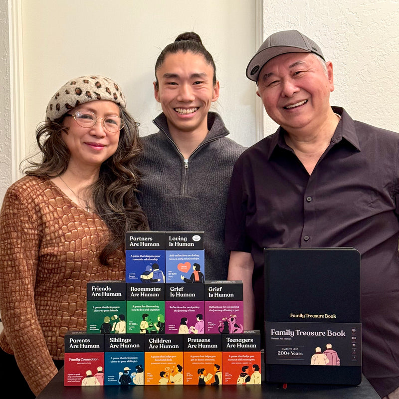 Three people smiling with a collection of human-themed card games and a family treasure book.